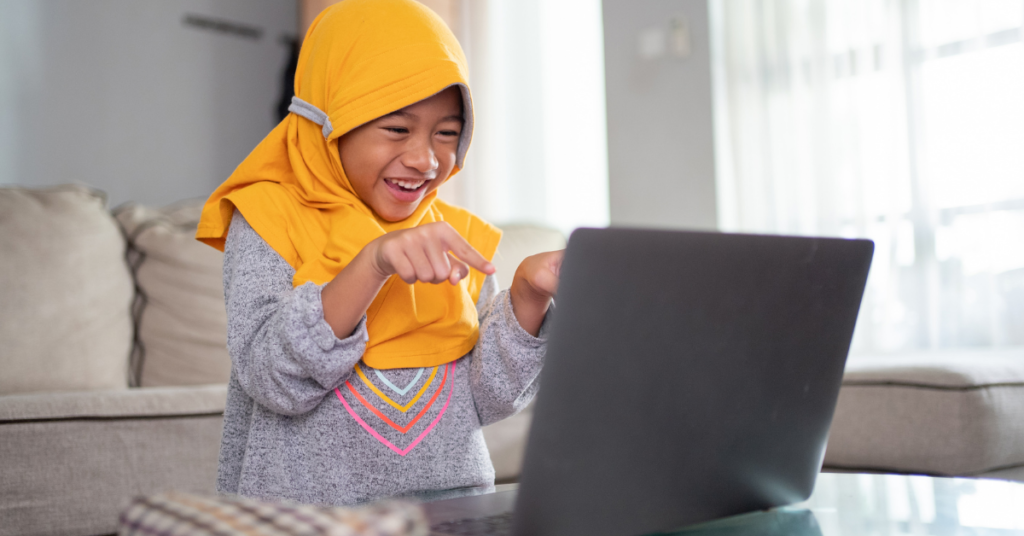 Child smiling and actively engaged during an online Quran class on a laptop at home